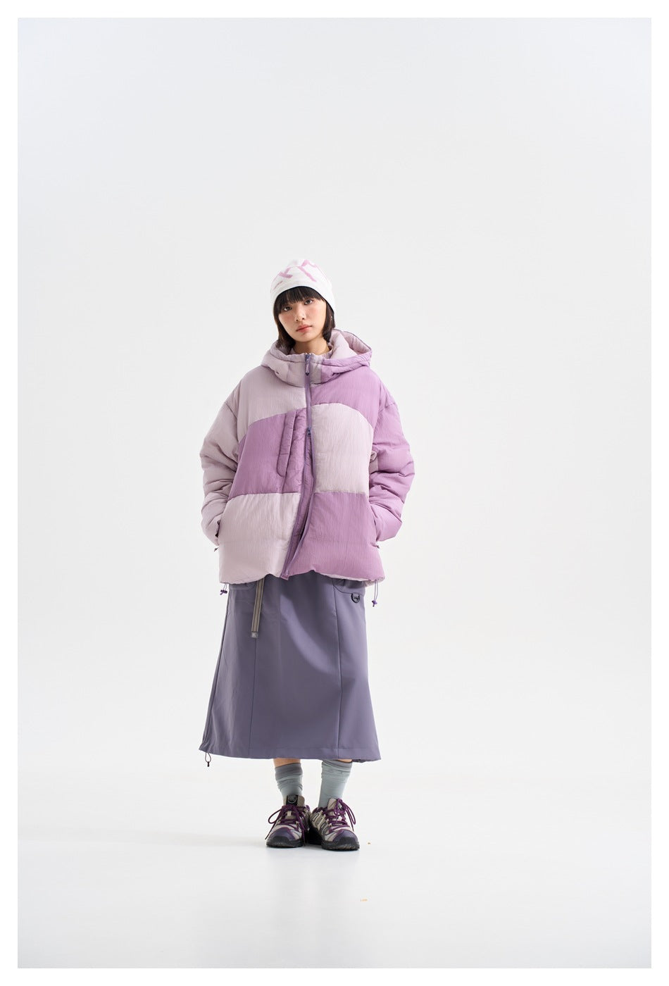 Front view of a model wearing a pale pink and lavender color-block hooded puffer jacket with a front zip.