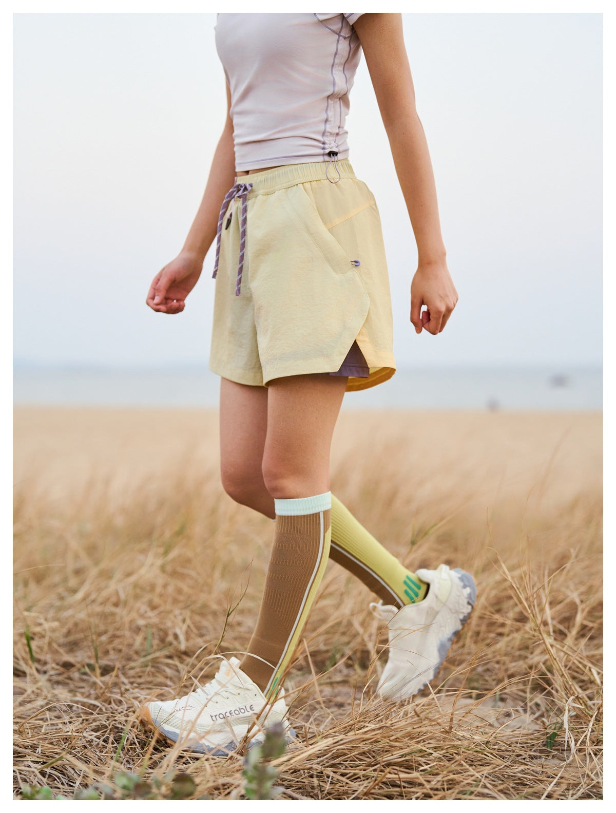 Cropped model wearing pale yellow running shorts with an elastic waist, patterned drawstring, and curved side panels.