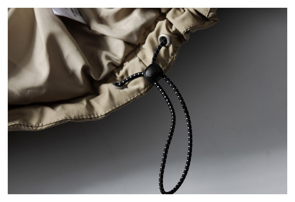 Close-up of the taupe jacket's black elastic drawcord, metal eyelet and cord lock.