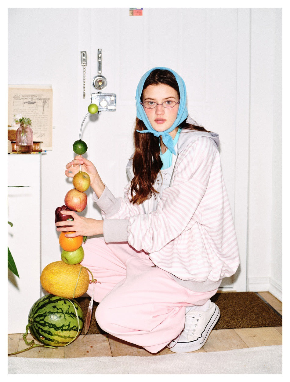 Model crouching in a pink and white striped hooded jacket with pink pants beside a stack of fruit