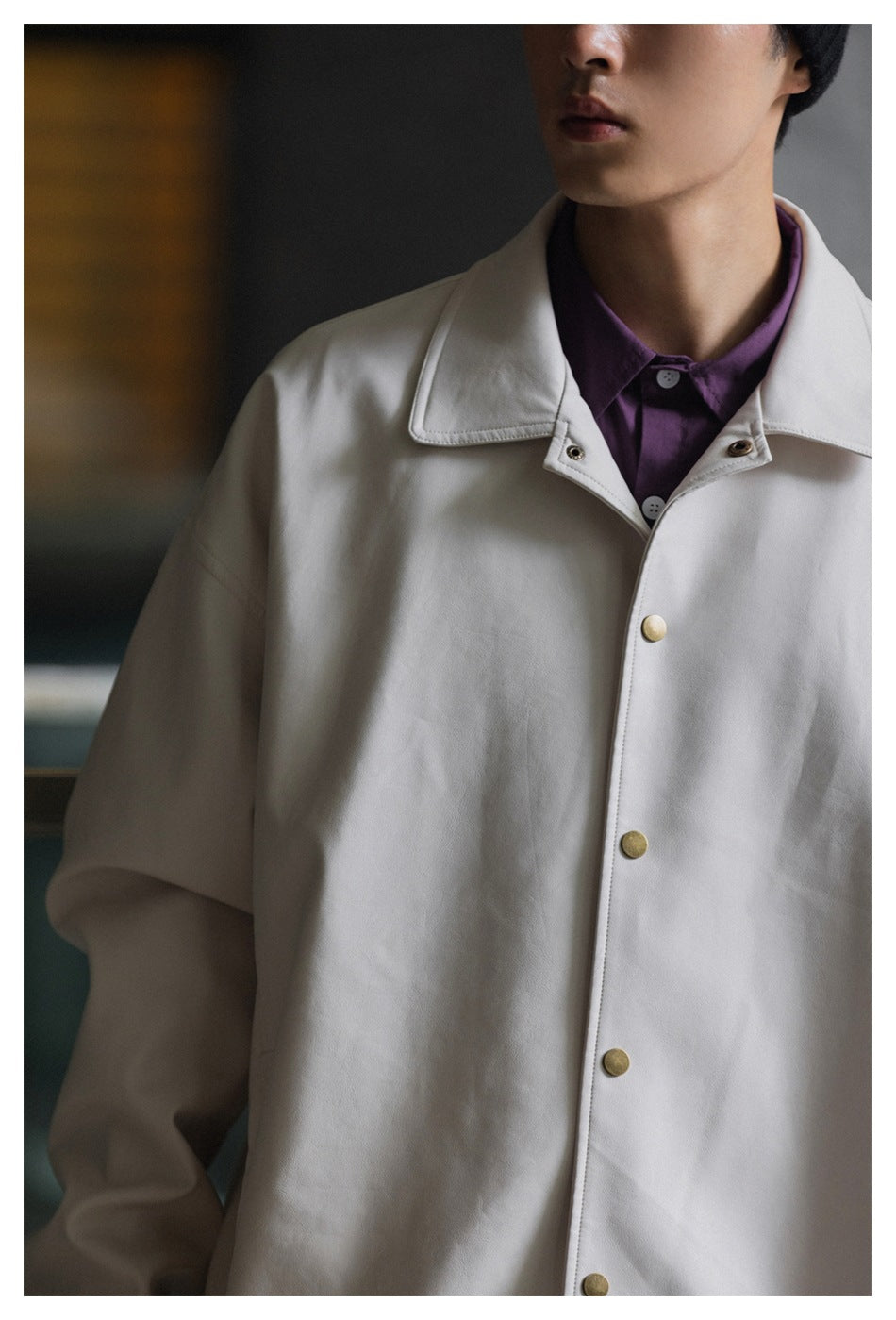 Close-up of a light beige jacket with a wide collar, brass-tone snap buttons, and a purple shirt underneath.