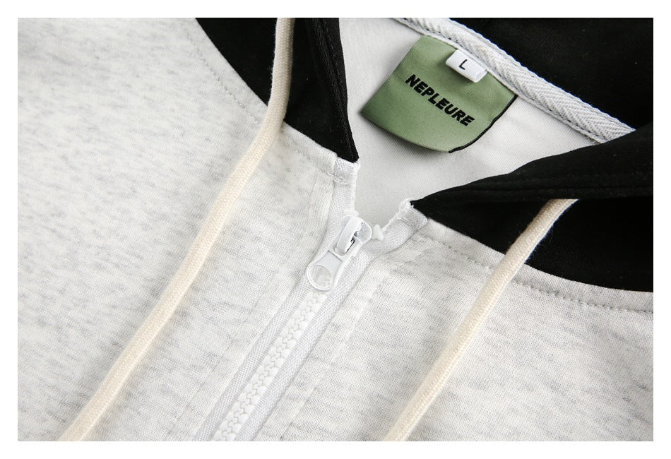 Close-up of the light gray hoodie’s white zipper, cream drawstrings, and neck label.