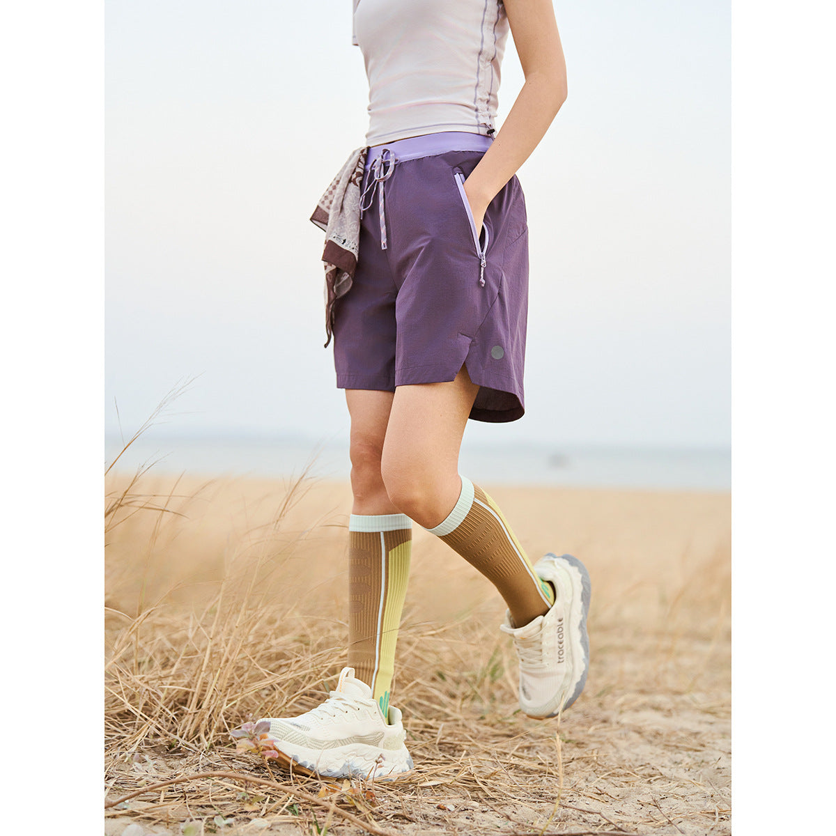 Cropped view of a person wearing purple running shorts with a drawstring waist and zip pockets outdoors.