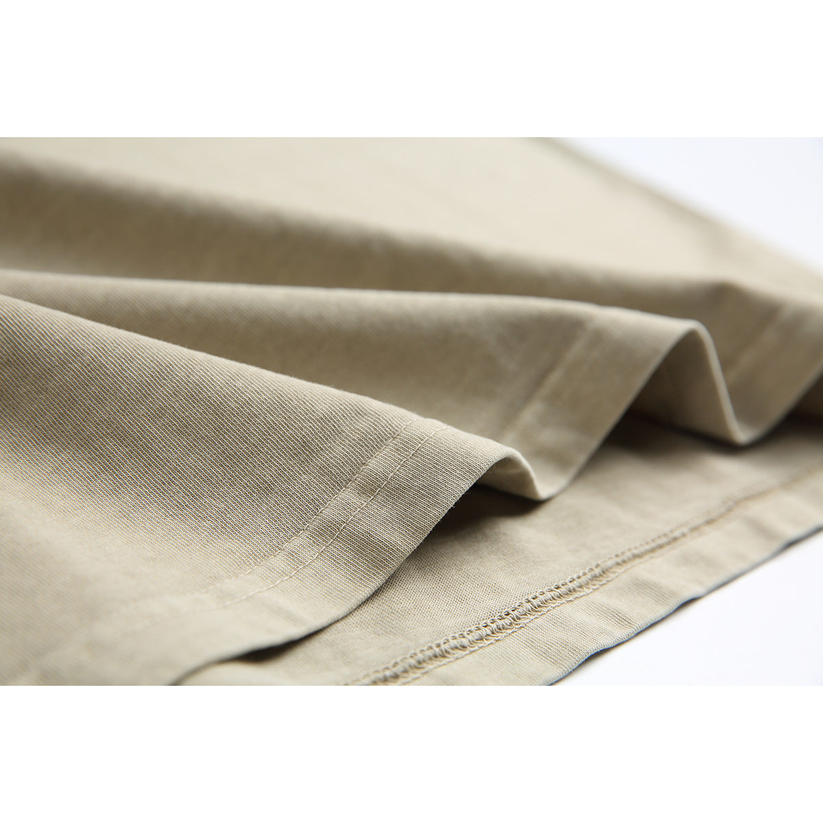 Close-up of the beige T-shirt's folded fabric and stitched hem.