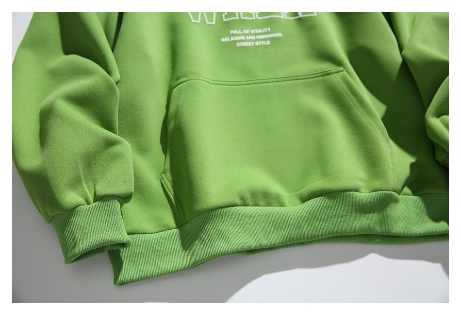 Close view of the green pullover's kangaroo pocket, ribbed hem and cuff, with part of the white chest print visible.
