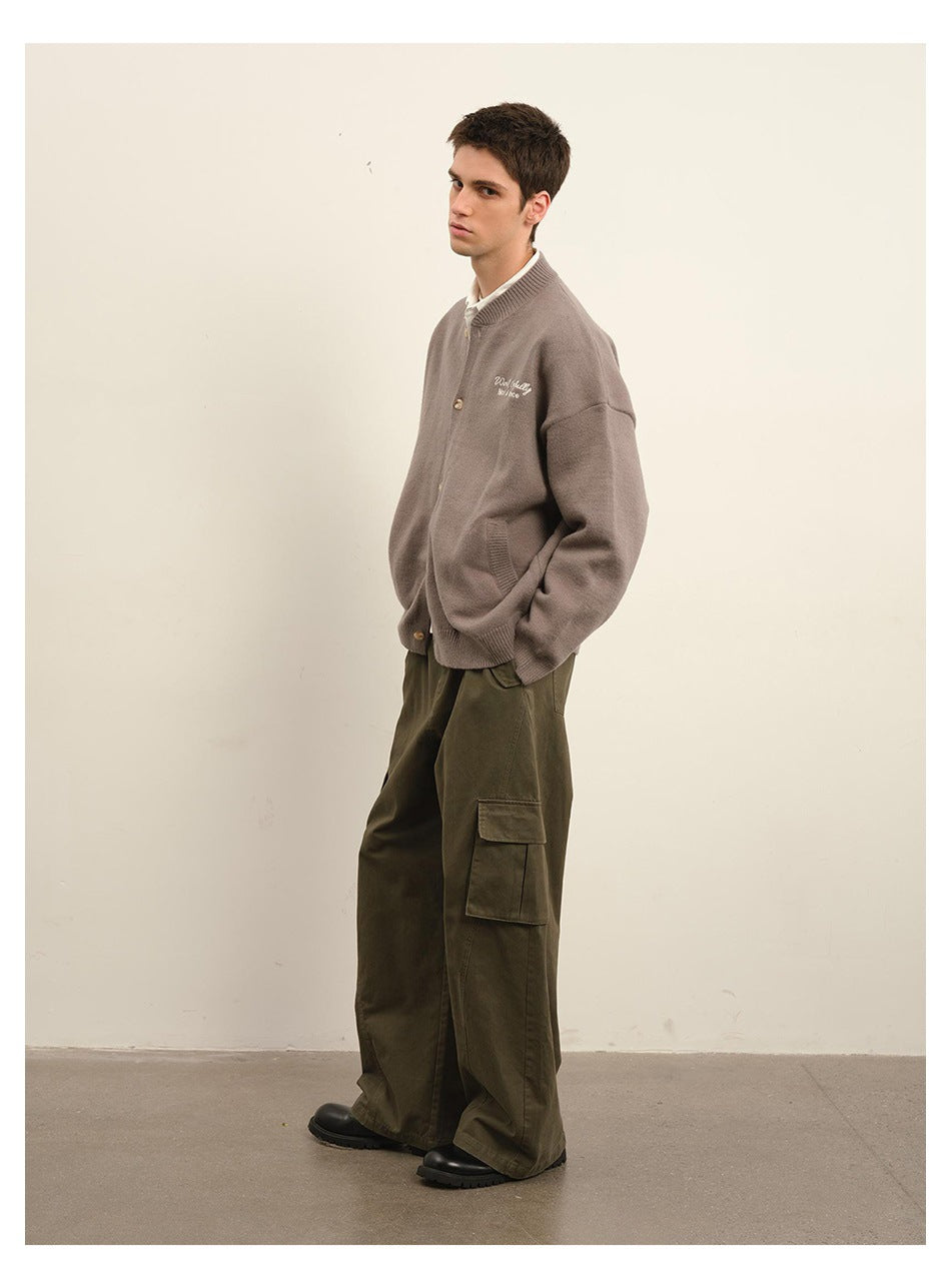 Full-length angled view of a model wearing a taupe cardigan with embroidered chest text and olive cargo trousers.