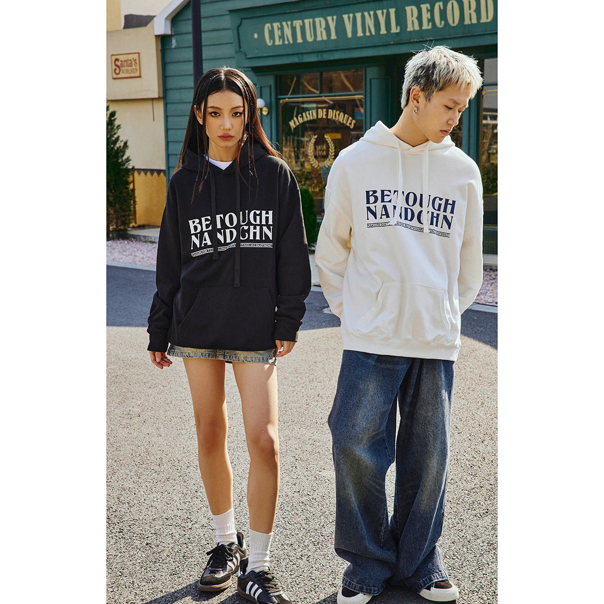 Two models pose in black and white graphic pullover hoodies; one wears a denim skirt and the other wide-leg jeans.