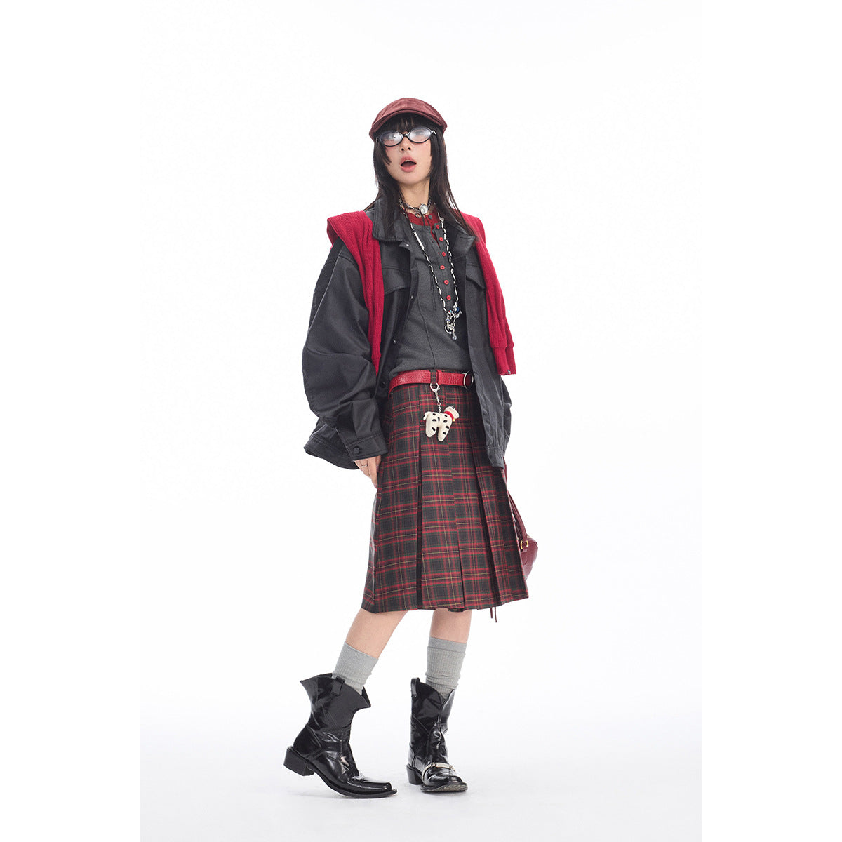 Full-length model wearing a charcoal jacket, red-and-black plaid skirt, red knit layer, and black boots.