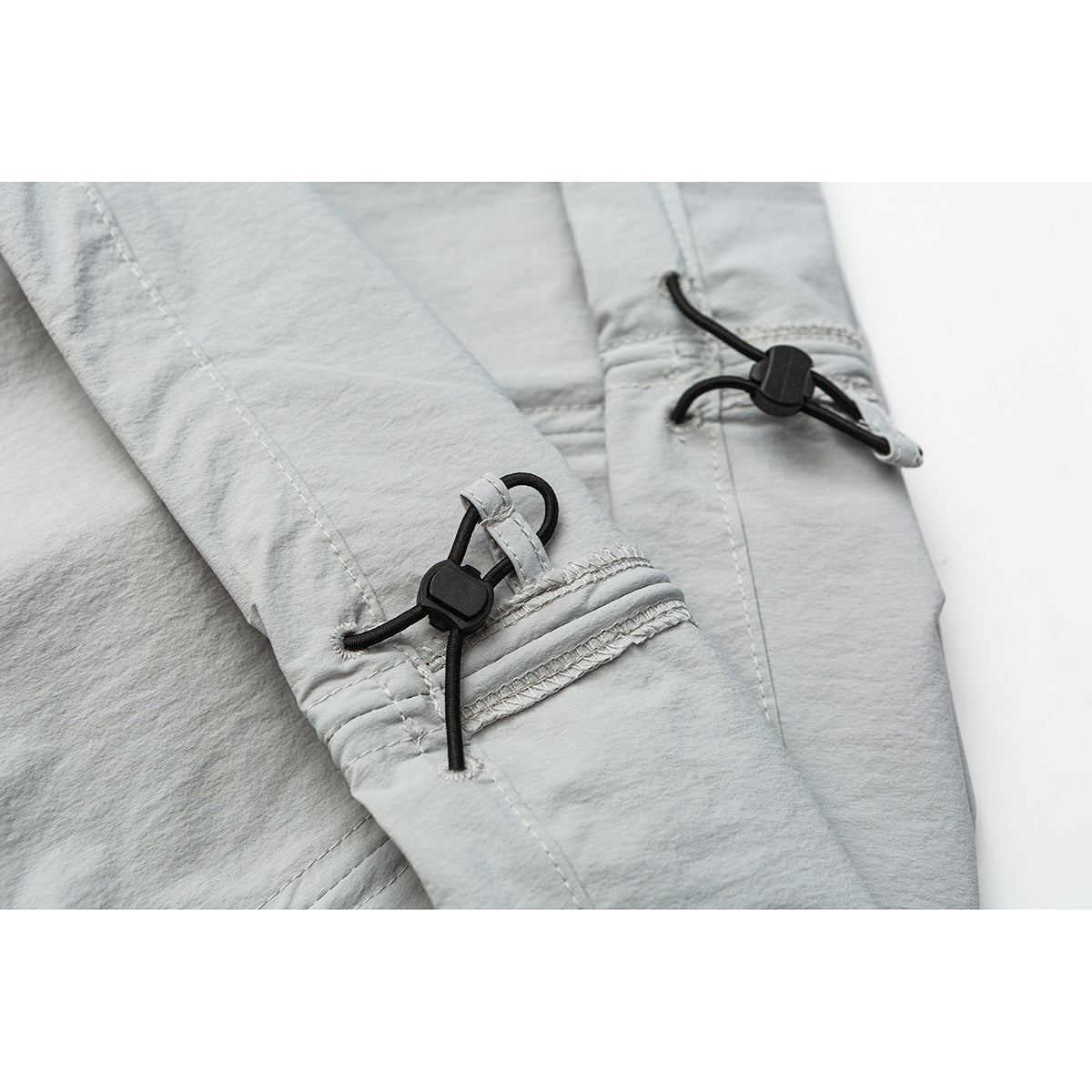 Close-up of black drawcord toggles and stitched details on light gray trouser legs.