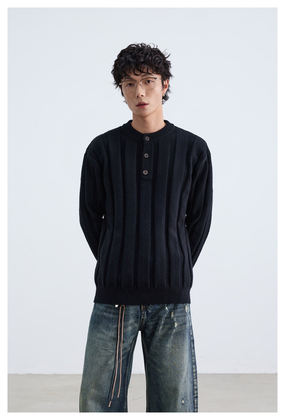 Model wearing a black ribbed sweater with a short button placket and crew neck, paired with distressed blue jeans.