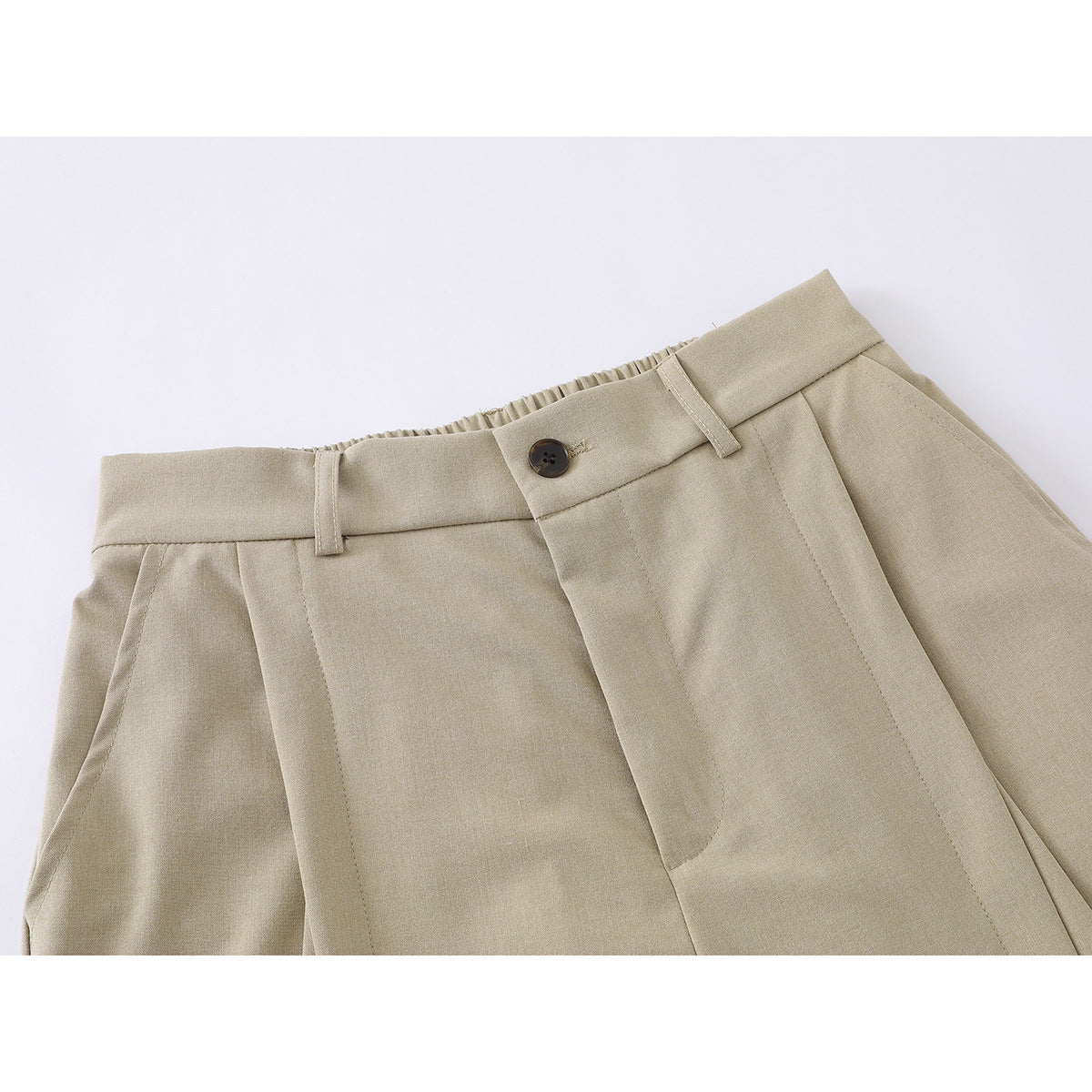 Close-up of beige shorts showing the buttoned waistband, belt loops, pleats and front fly.