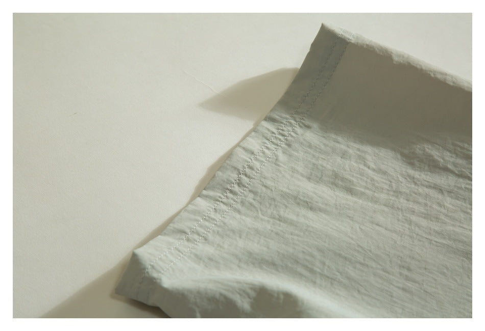 Close-up of the pale sage jacket's stitched hem and softly wrinkled fabric.
