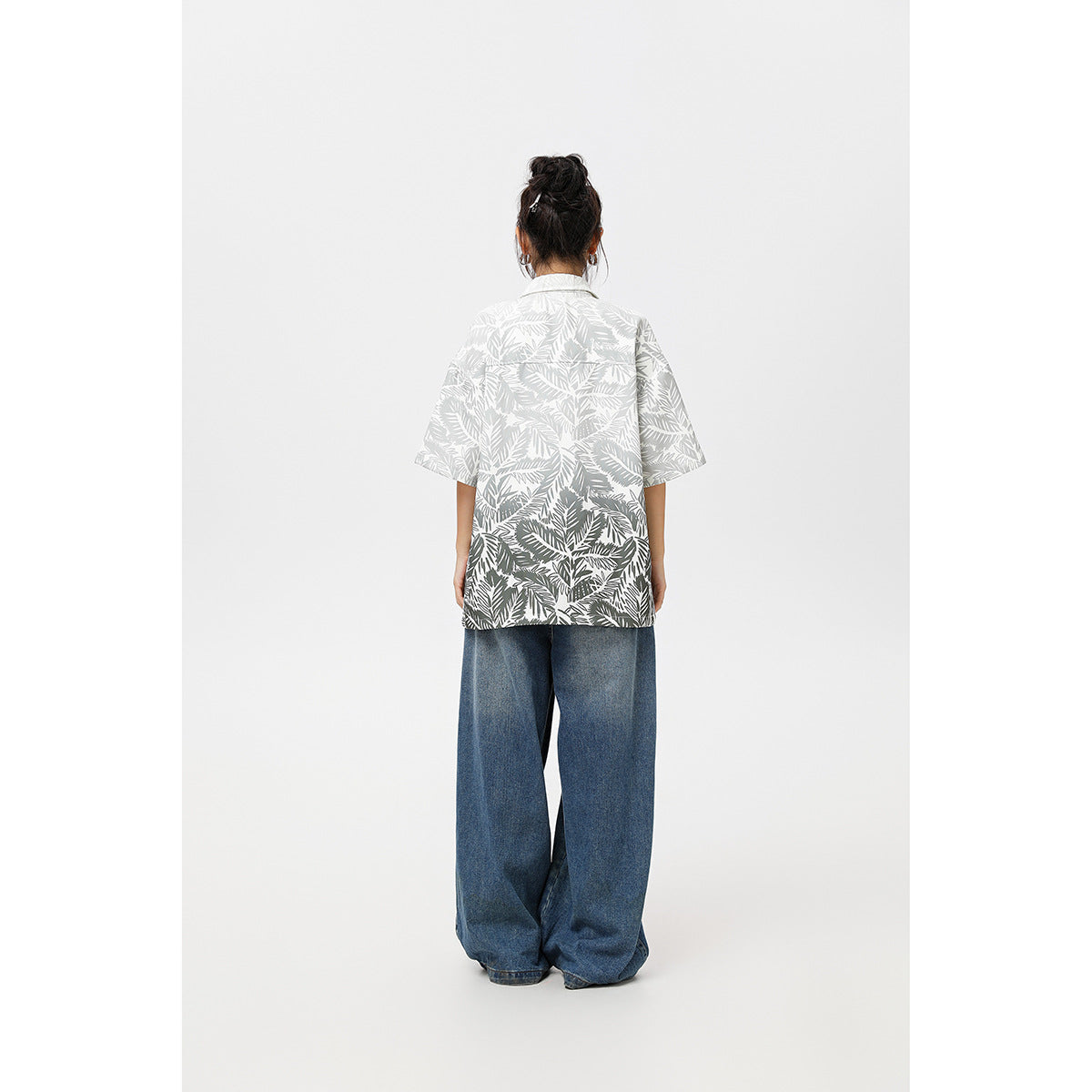 Back view of a model wearing a gray-and-white tropical leaf print short-sleeve shirt and wide blue jeans.