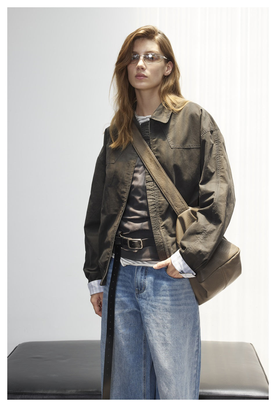 Three-quarter view of a model wearing a dark olive oversized jacket with chest pockets and wide-leg blue jeans.