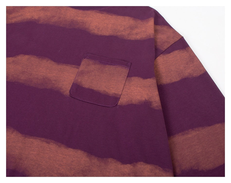 Close-up of the plum sweatshirt's chest pocket, set against broad rust-brown wavy stripes.