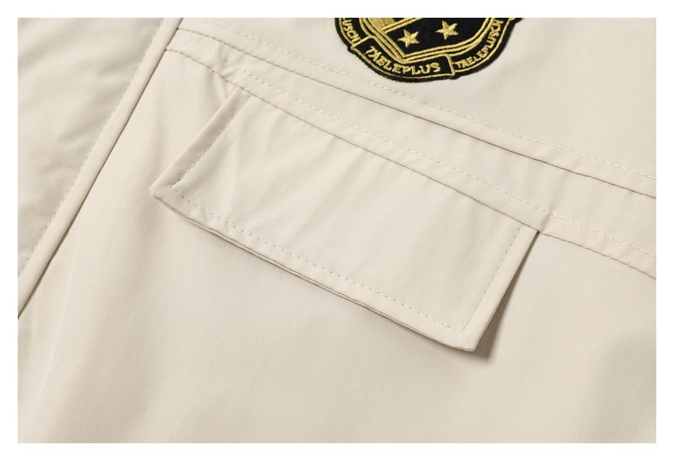 Close-up of a cream jacket's flap pocket and black-and-gold embroidered crest.
