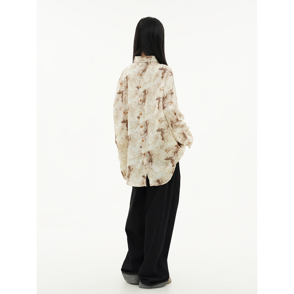 Rear view of a model wearing an oversized cream and brown abstract-print button-up shirt with black wide-leg jeans.