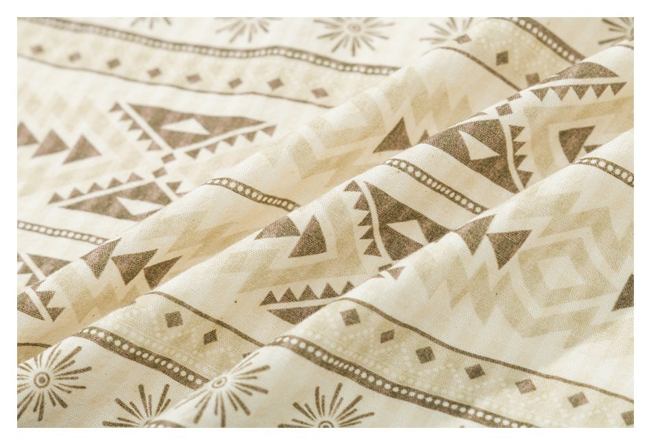 Close-up of cream fabric with brown geometric triangles, dotted bands, and sunburst motifs.