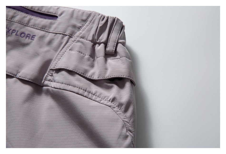 Close-up of pale mauve trousers showing a gathered waistband, belt loop, and layered side pocket.