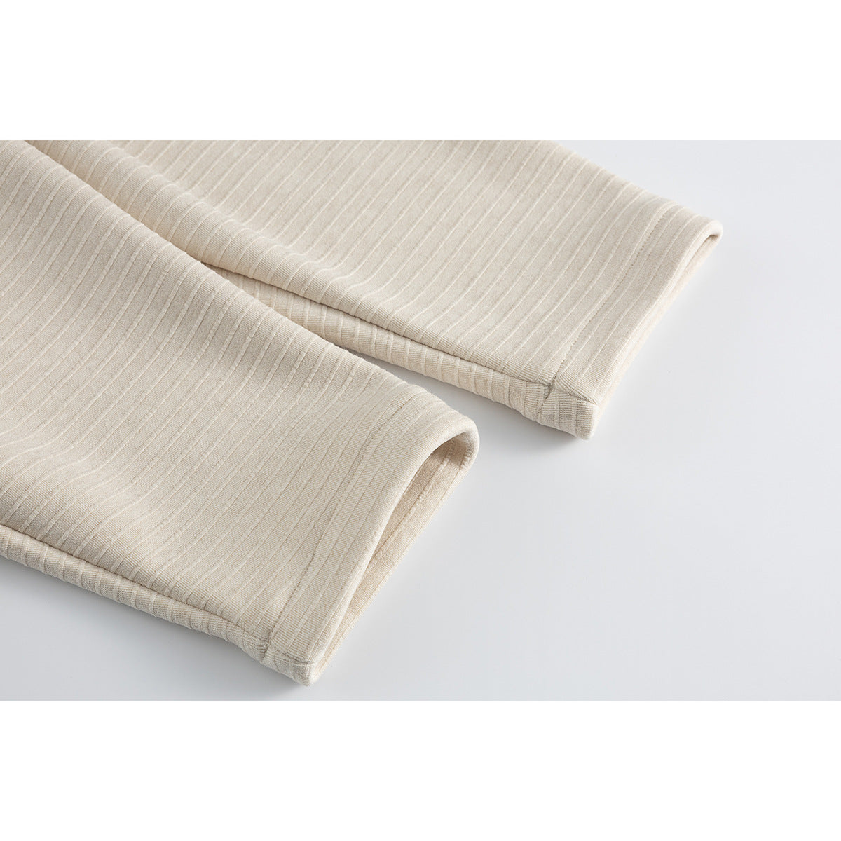 Close-up of two cream rib-knit jacket sleeve cuffs with fine horizontal texture.