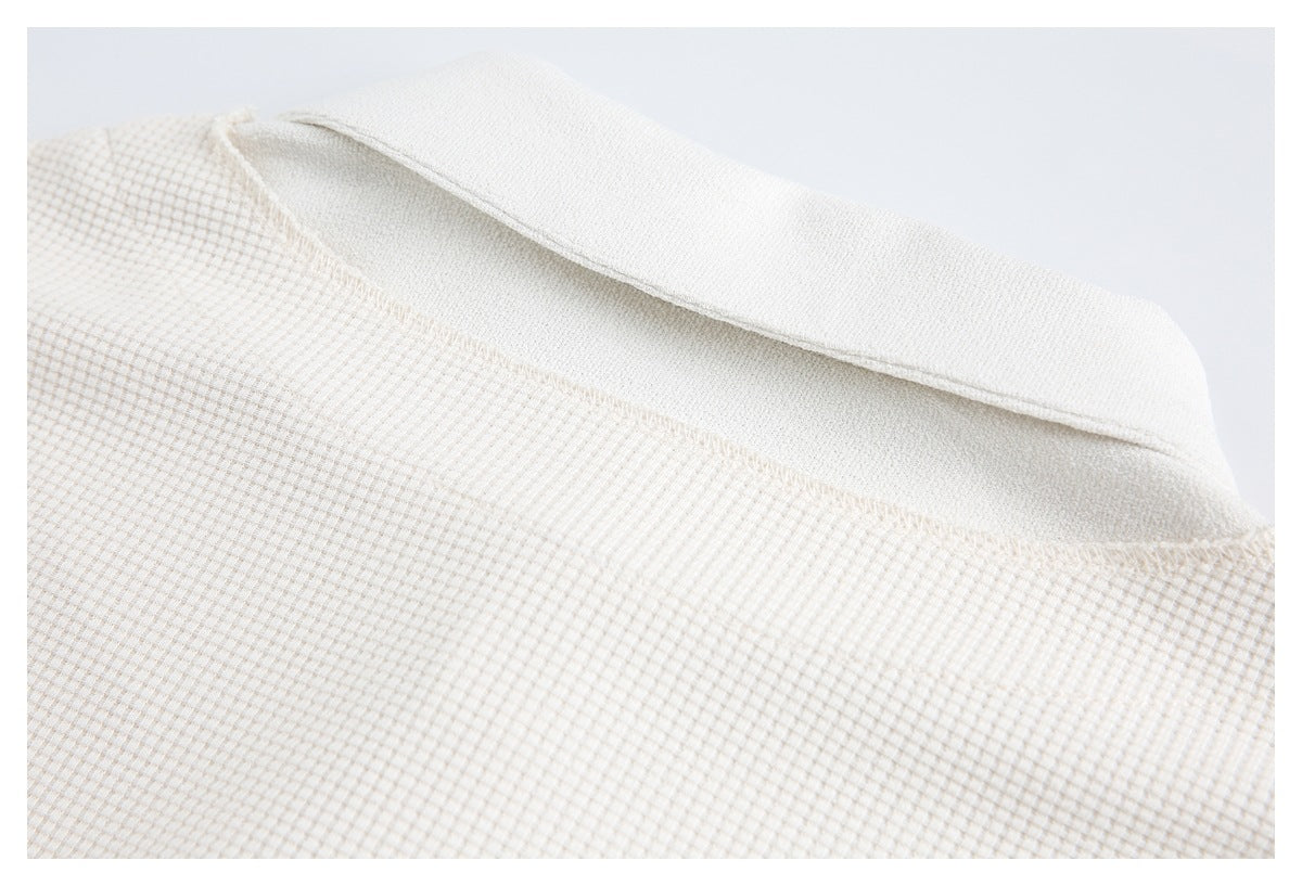 Close-up of the off-white waffle-knit garment's folded collar and neckline stitching.