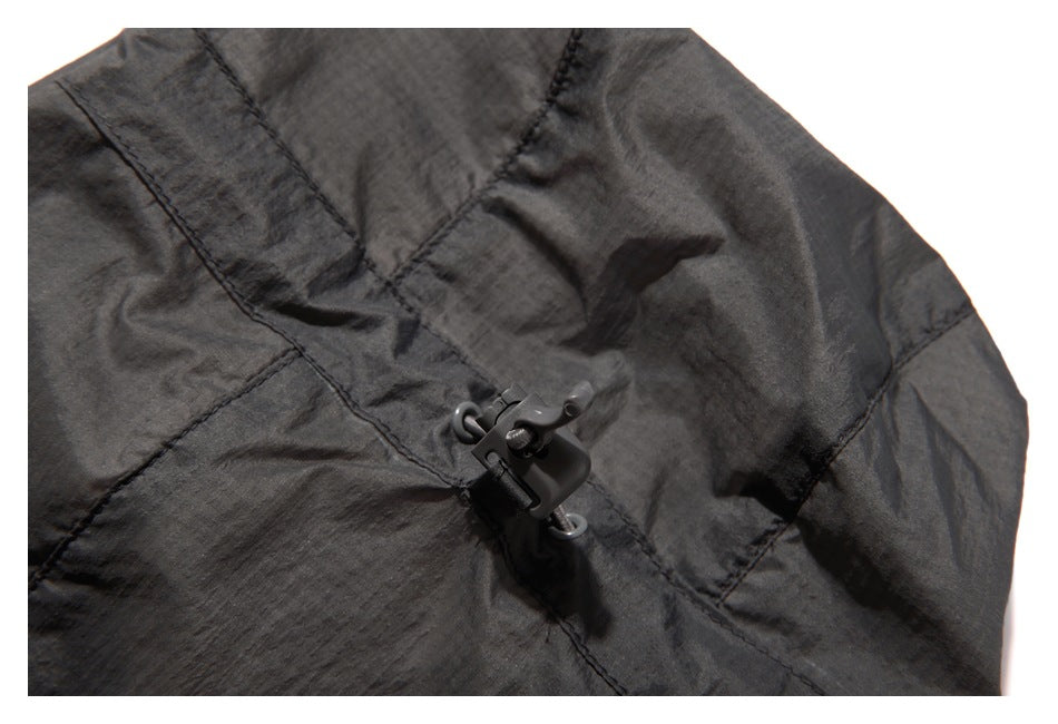 Close-up of a dark charcoal garment with a small plastic cord-adjustment toggle at a stitched seam.