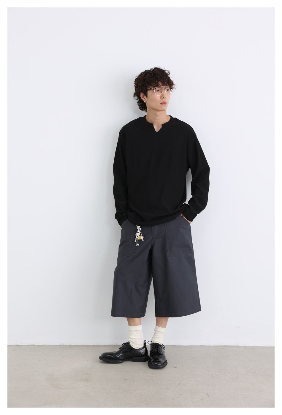 Model wearing black ribbed long-sleeve top with notched V-neck and gray wide-leg shorts, full-length view