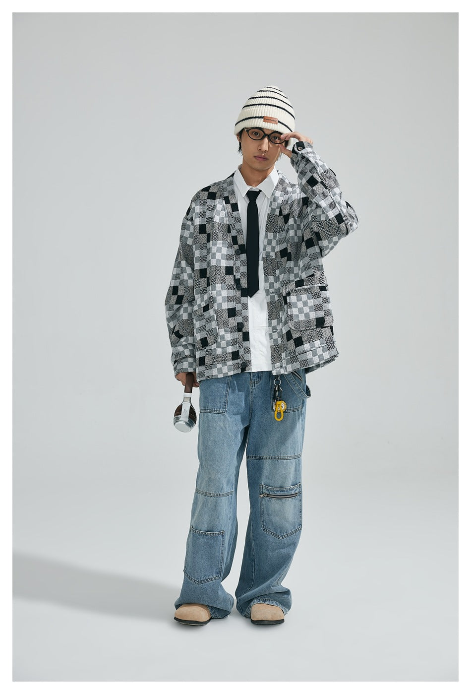 Model wearing the gray checkerboard button-front jacket over a white shirt and tie with wide-leg light-wash jeans