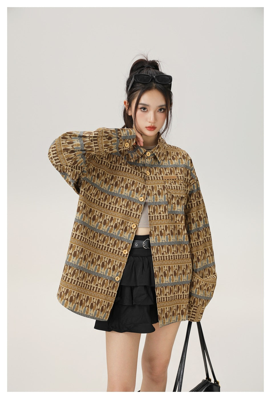 Close front view of a model wearing an oversized brown geometric-pattern button-up jacket with blue-gray stripe accents.