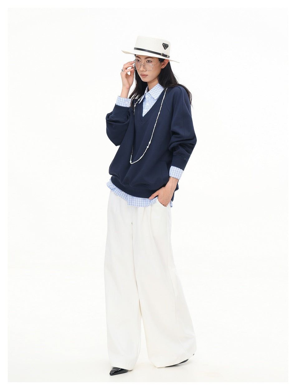 Full-length front view of a model wearing a navy V-neck sweatshirt over a blue checked shirt and white wide-leg trousers.