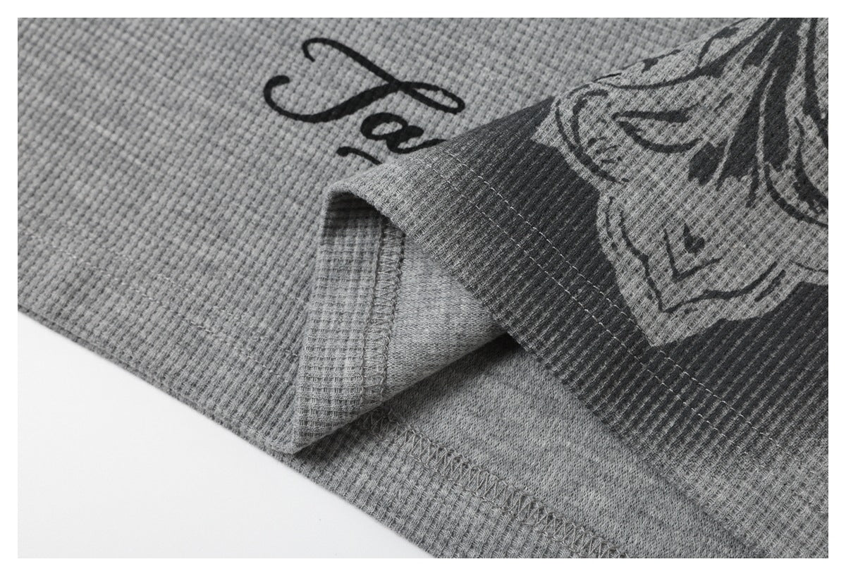Folded edge of a gray waffle-knit top, showing the stitched hem and part of its printed design.