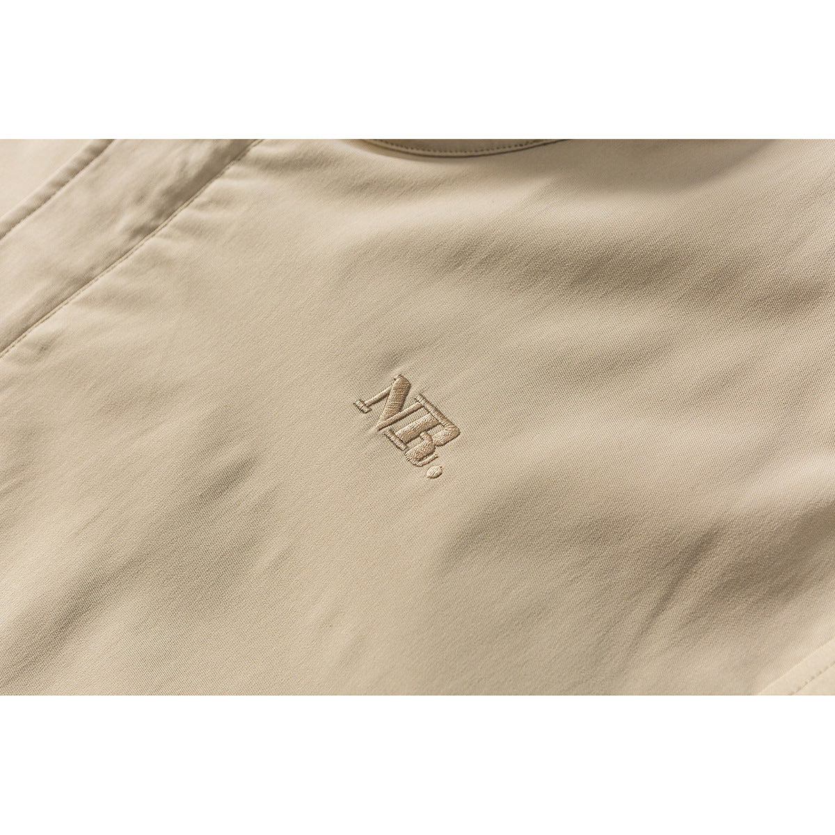 Close-up of a small tonal embroidered emblem on tan jacket fabric.