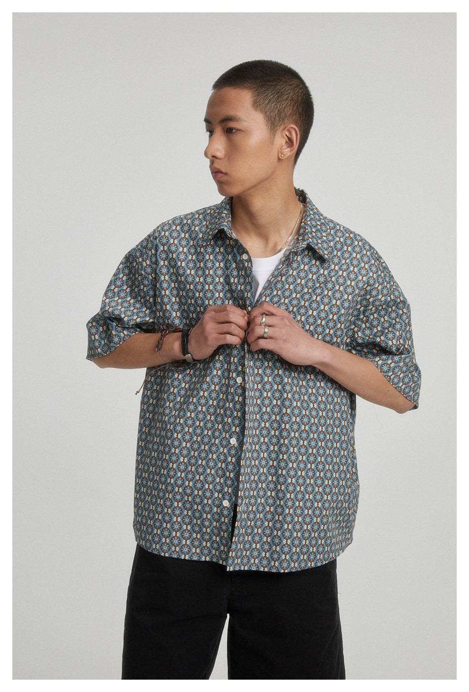 Model facing slightly sideways in a blue floral short-sleeve button-up shirt, holding its front near the buttons.