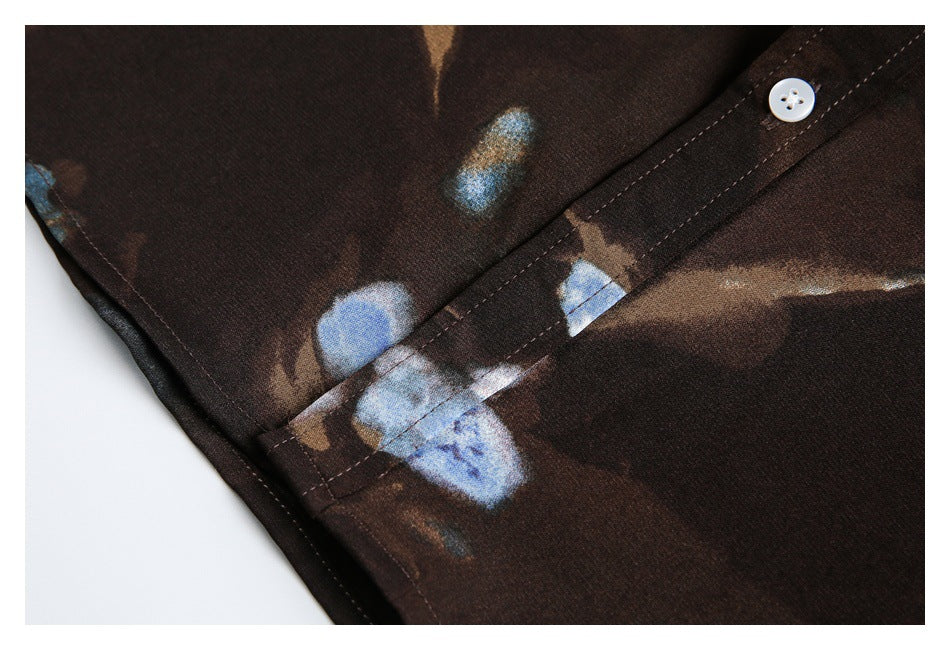 Close-up of a dark brown shirt with abstract blue and tan print, showing a white button and stitched placket.
