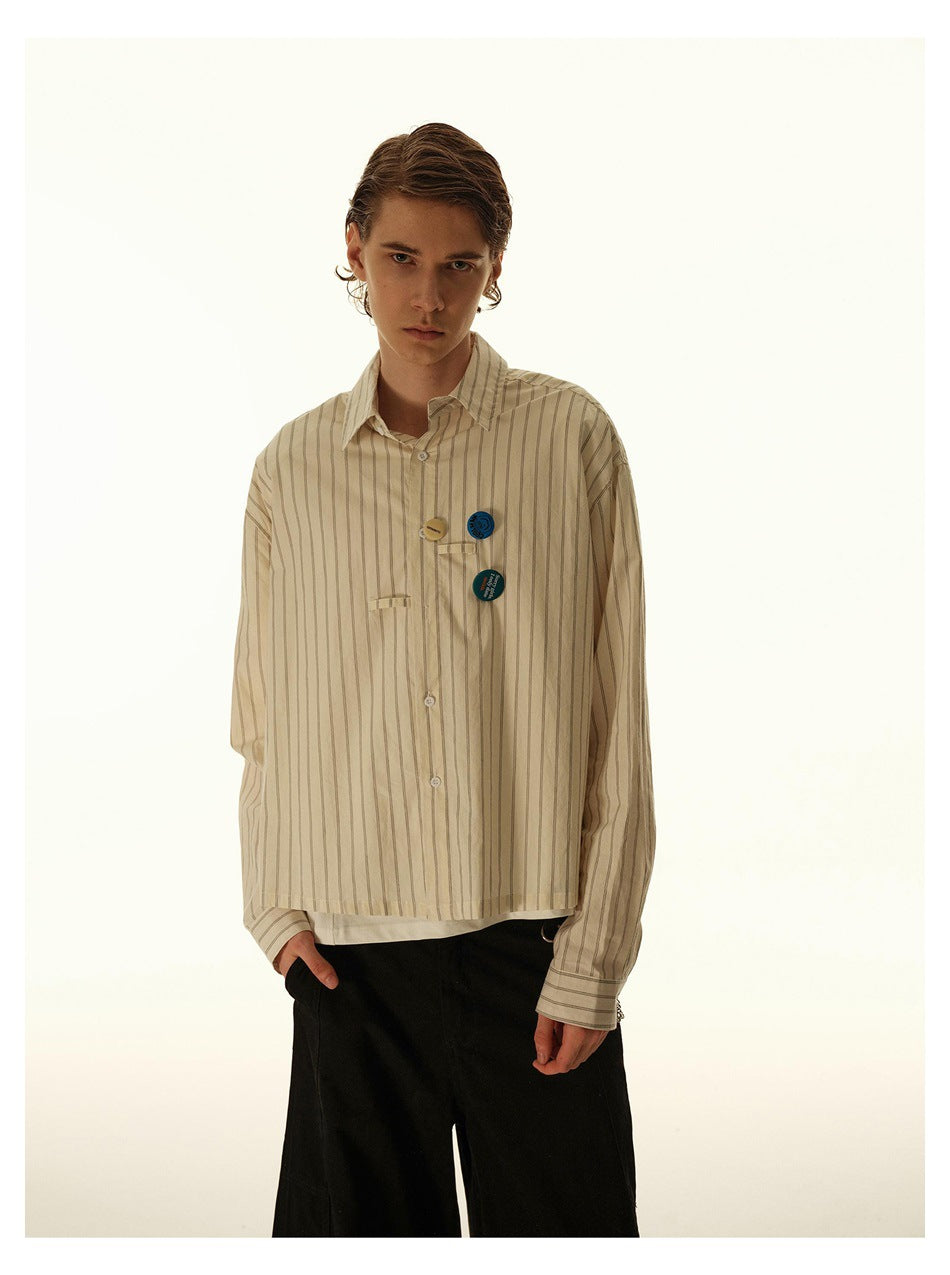 Model wearing a beige striped button-up shirt with decorative pins, shown from the front without the tie.