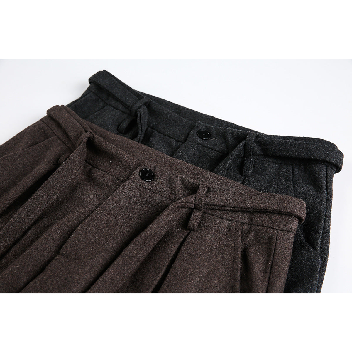 Close-up of brown and charcoal pleated trousers with belt loops, buttons, and front pockets.
