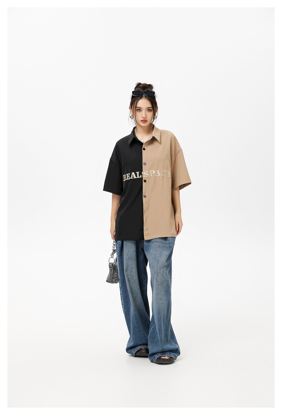 Model wearing an oversized short-sleeve button-up shirt split black and tan, with cream REAL SPACE lettering and wide-leg