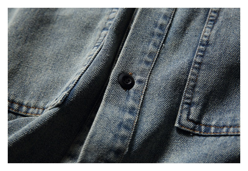 Close-up of a faded blue denim shirt front, showing the button placket and edge of a chest pocket.