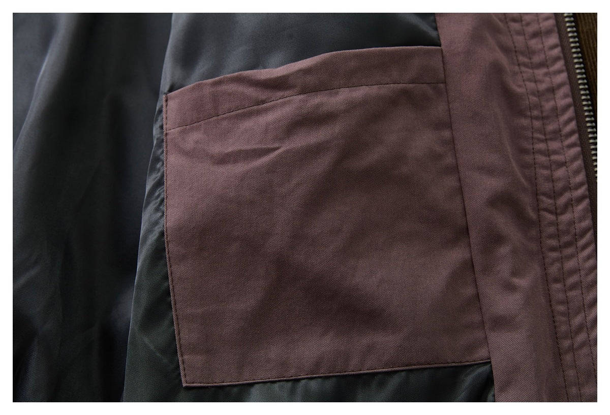 Close-up of a large plum-brown patch pocket against dark jacket lining, beside a zipper and stitched placket.