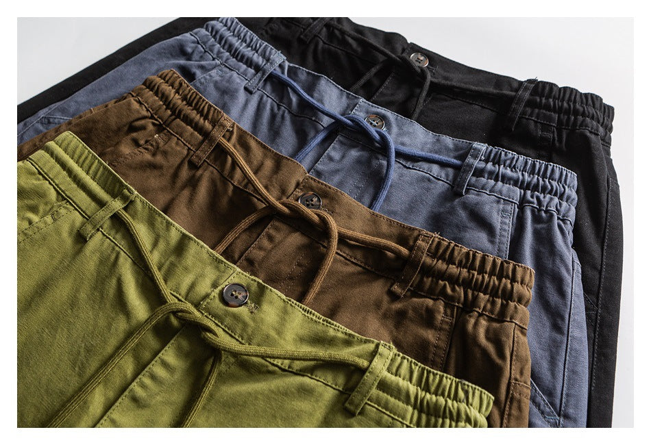 Close-up of trousers in olive, brown, slate blue, and black, showing their waistbands, drawstrings, buttons, and pockets.