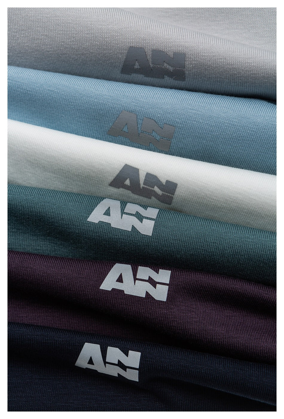 Several folded garments in gray, blue, white, teal, plum, and dark navy, each with a small logo.
