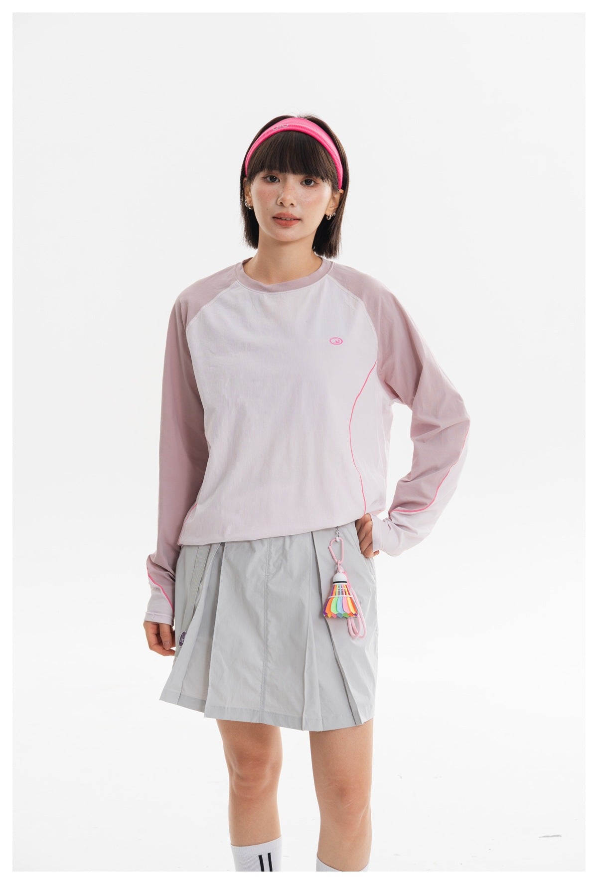 Model wearing a pale pink and white long-sleeve top with a light gray pleated skirt, shown from the front.