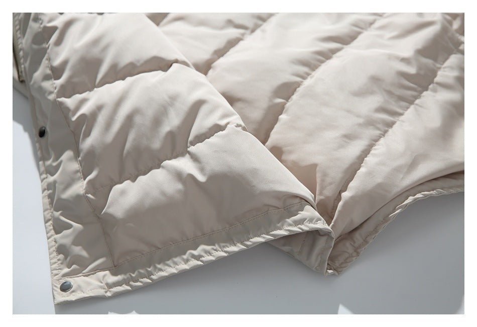 Close-up of a cream padded jacket's quilted panels, snap fastener, and finished hem.