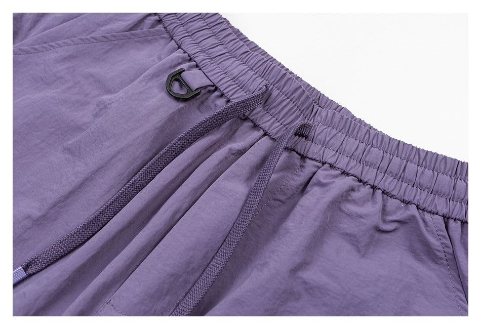 Close-up of purple pants showing the elastic waistband, front drawcords, pocket seam, and black clip.