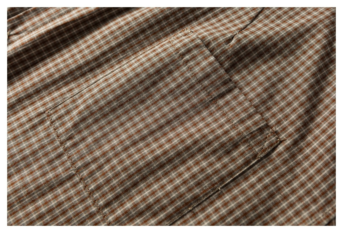 Close-up of a rectangular pocket on rust, gray, and white checked shirt fabric.