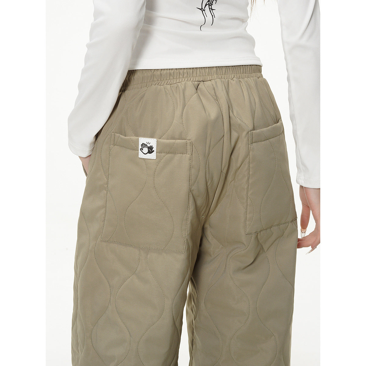 Close-up of khaki quilted pants showing the elastic back waist, large pockets and a small hand-icon patch.