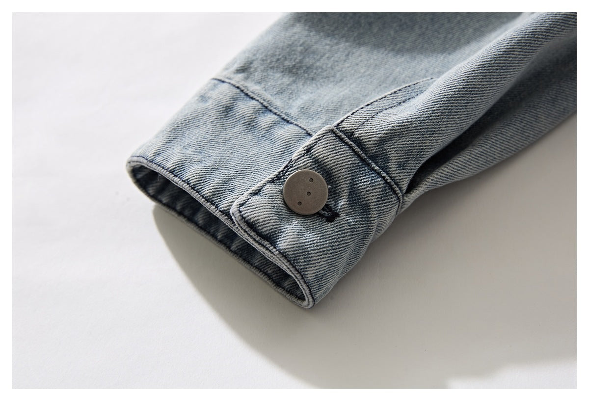 Close-up of a light blue washed denim jacket sleeve cuff with a large dark button.