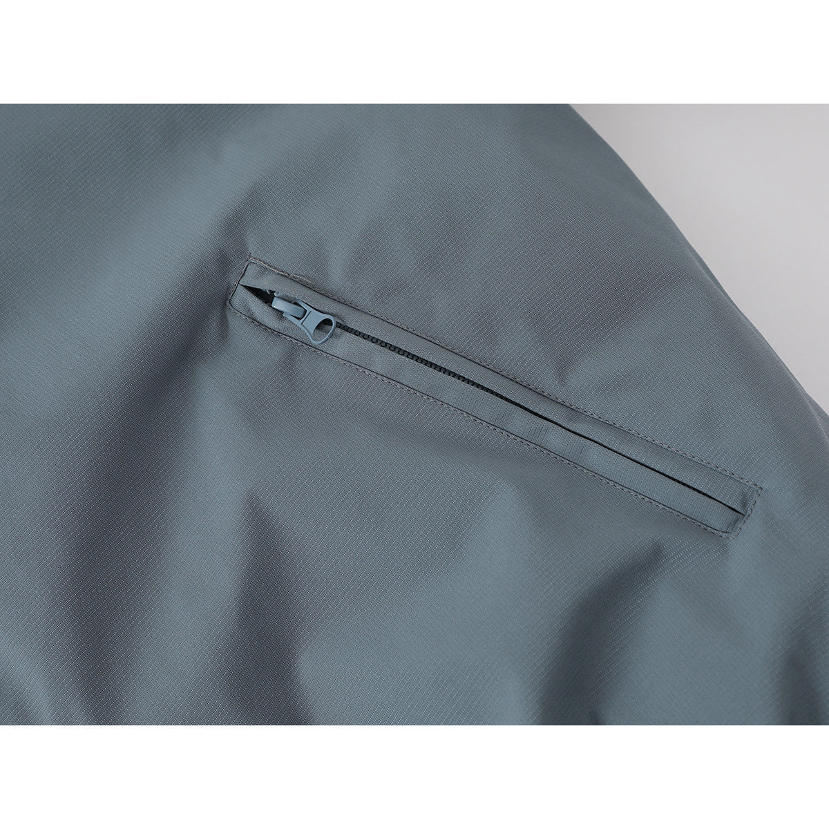 Close-up of a slanted zip pocket on a slate blue-gray jacket.