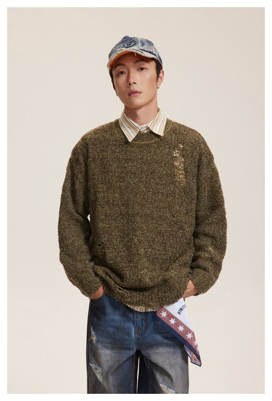 Front view of a model in an olive-brown mottled sweater with distressed openings and a striped shirt collar.