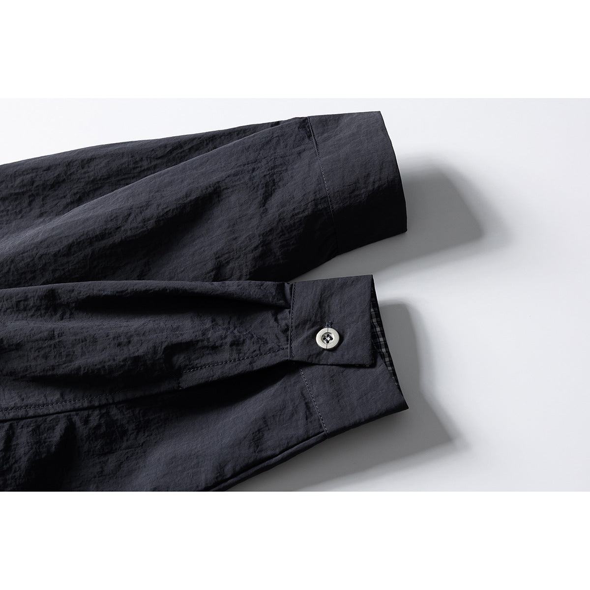 Close-up of a dark charcoal shirt sleeve and buttoned cuff, with a glimpse of check lining.